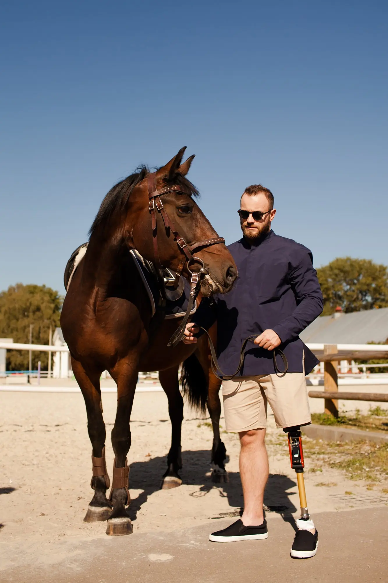 Man with a leg prosthesis holding a horse by the reins